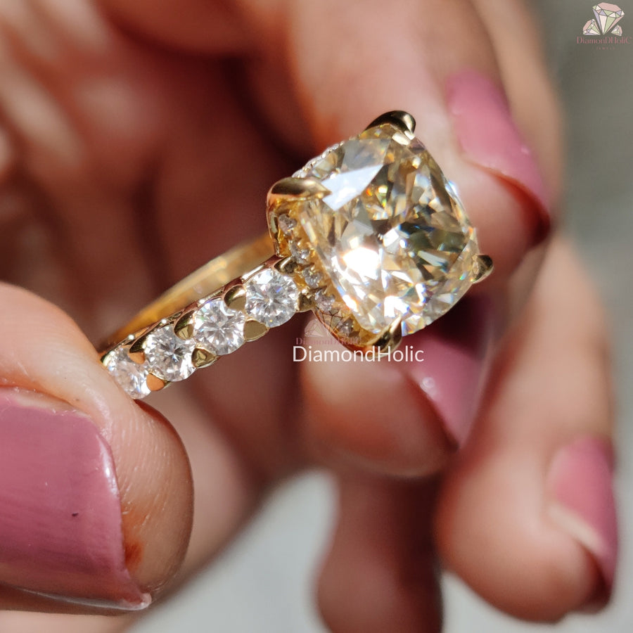 Diamond Holic Cushion Cut Moissanite Wedding Ring with gold band and side stones held between fingers