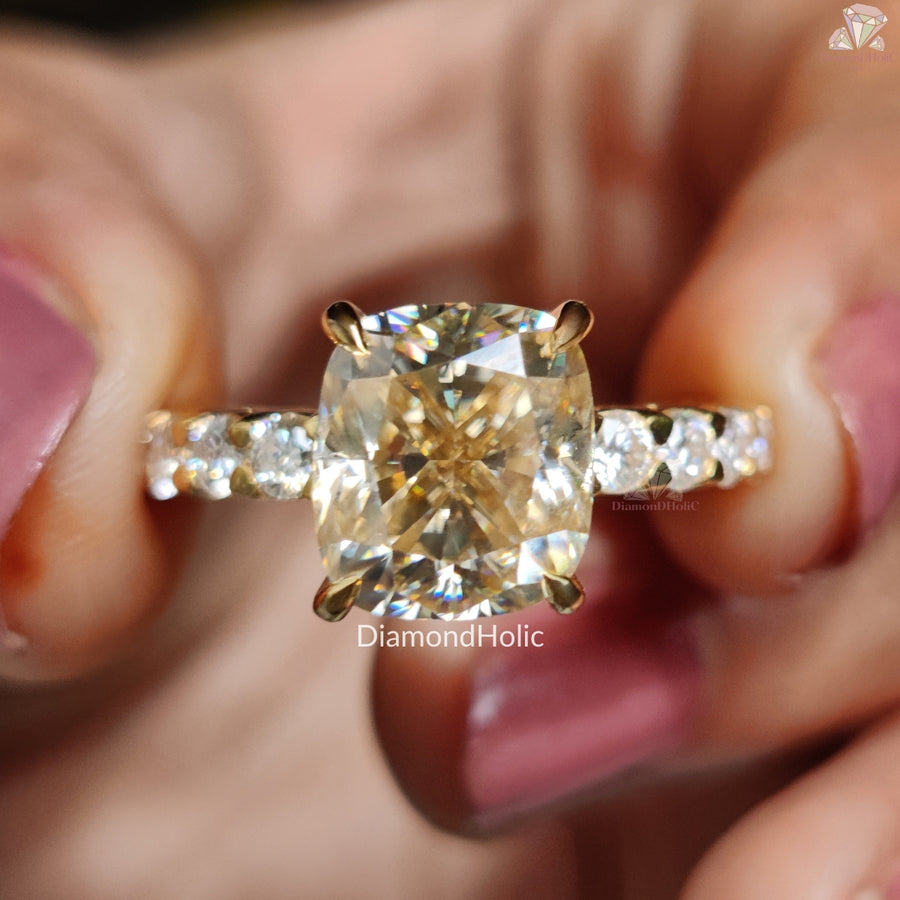 Diamond Holic Cushion Cut Moissanite Wedding Ring with gold band and side diamonds held between fingers