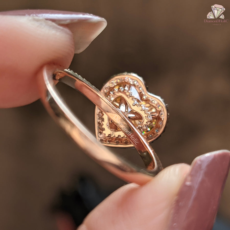 Rose gold heart-shaped ring held by a hand with a blurred background